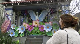 A woman looks at a New Orleans house, which has been decorated with giant flowers and birds to resemble a Mardi Gras float.
