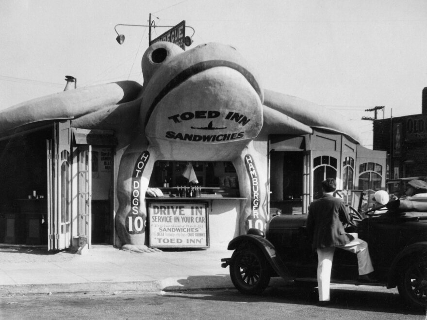 This toad-shaped sandwich bar called the Toed In, near Los Angeles in 1939, allowed you to grab a bite to eat while your car got serviced. There's a lot of wordplay going on here: the toad-shaped building, the "towing in" of the car, and the stepping or "toeing" in for a snack. Good job, punsters!