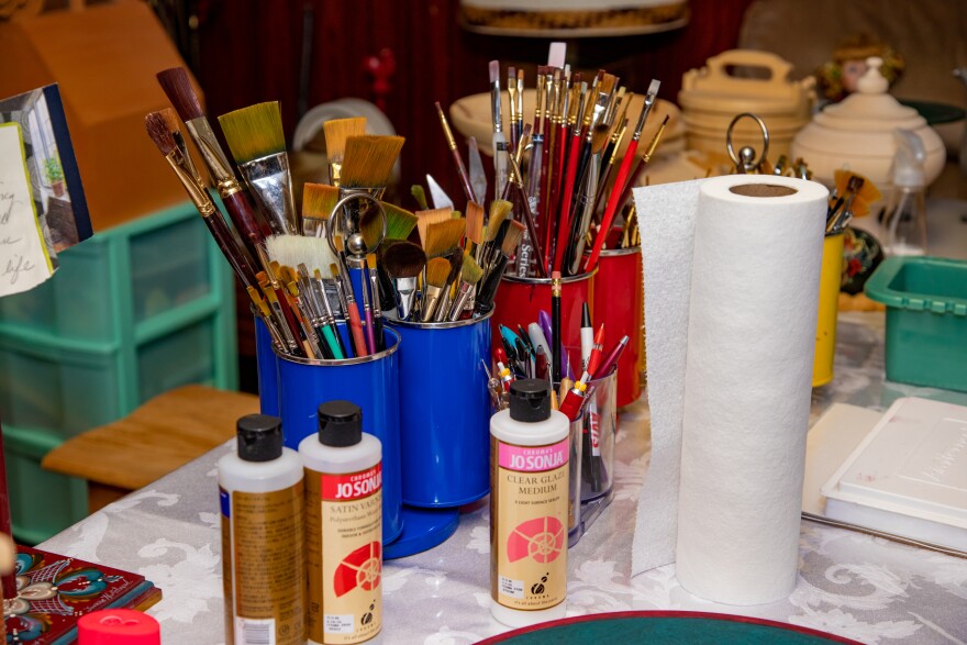 Paintbrushes in cups and acrylic paints in their bottles with a roll of paper towels. 