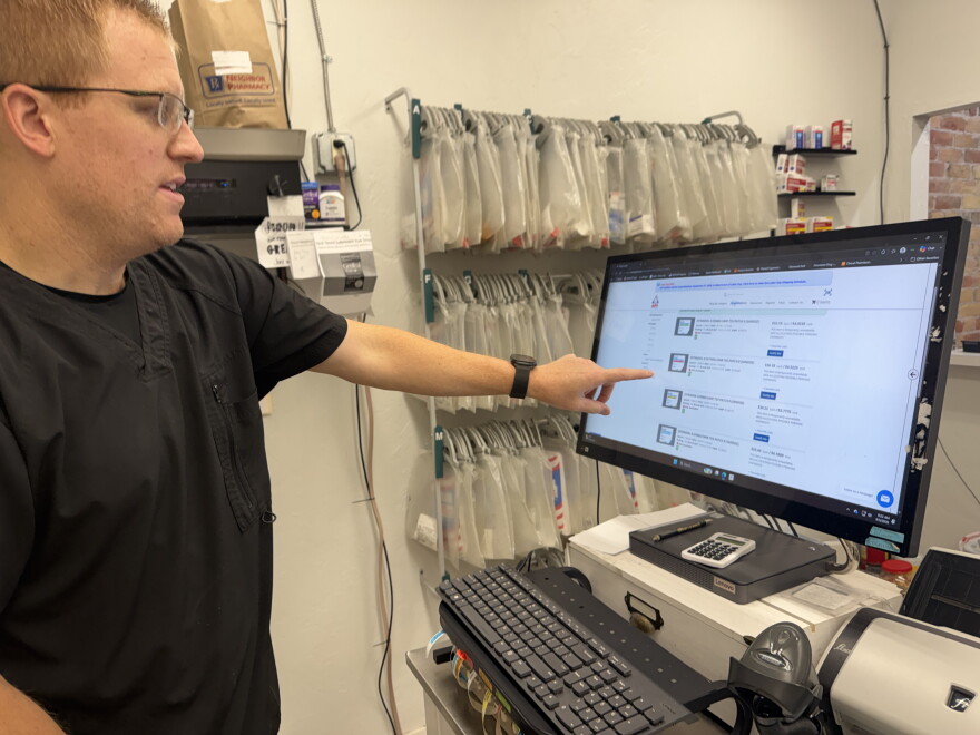 Jason Gotzinger señala su computadora detrás del mostrador de Downtown Drug, en Glenwood Springs, el 5 de septiembre de 2026. Está revisando su inventario de parches de estrógenos procedentes de diferentes distribuidores.