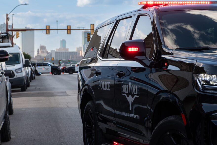 A photo of a black Fort Worth police SUV parked on a city street with the Fort Worth skyline in the background.