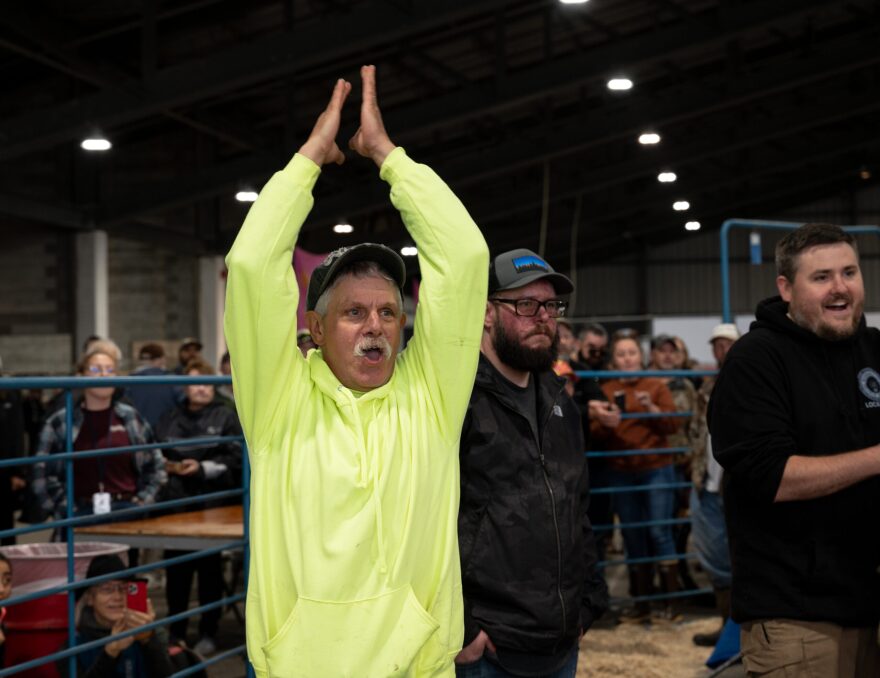A man in a neon green sweatshirt waves his arms in celebration.