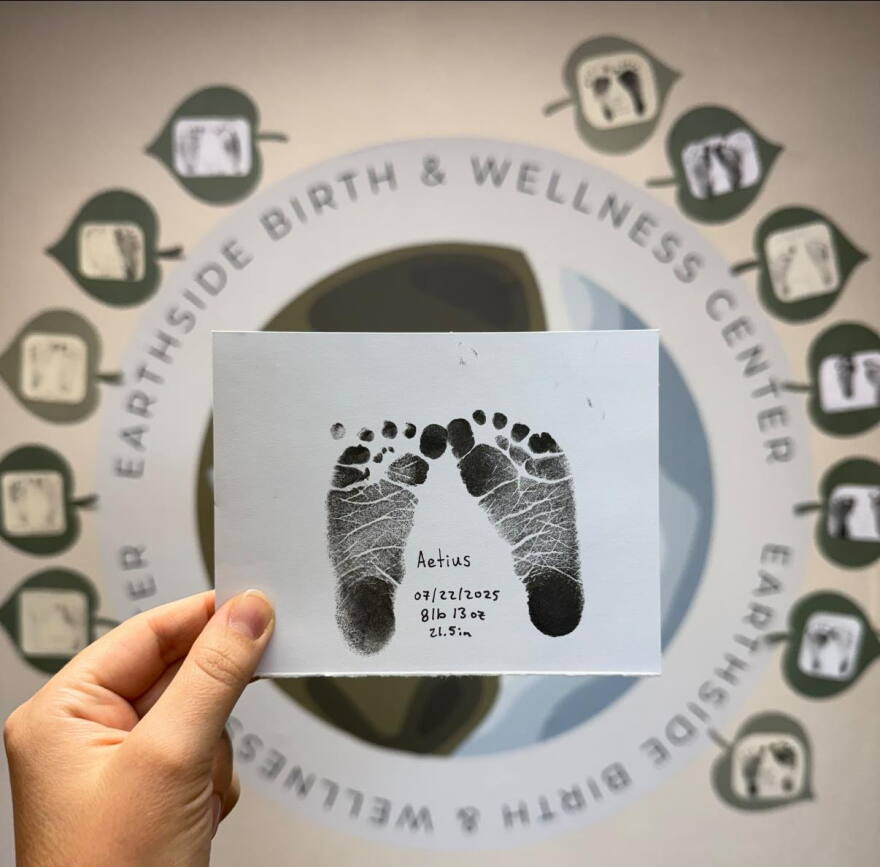 A hand is shown holding up a piece of paper showing baby ink footprints.