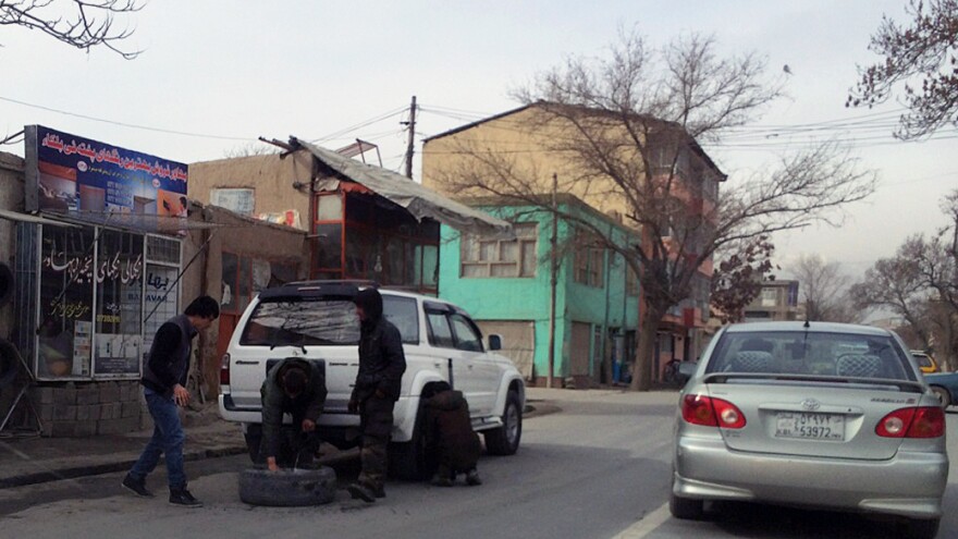Afghans change a tire on the side of a street in Kabul's 10th District, where police have been puncturing tires at night to prevent car theft.