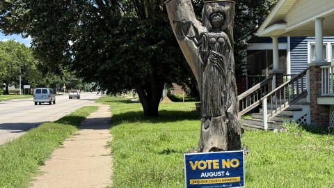 A keep our courts impartial sign sits in front of a tree stump carved lady justice — a blindfolded symbol which represents impartiality and objectivity — something that people who oppose the amendment worry could be lost if justices are directly elected.