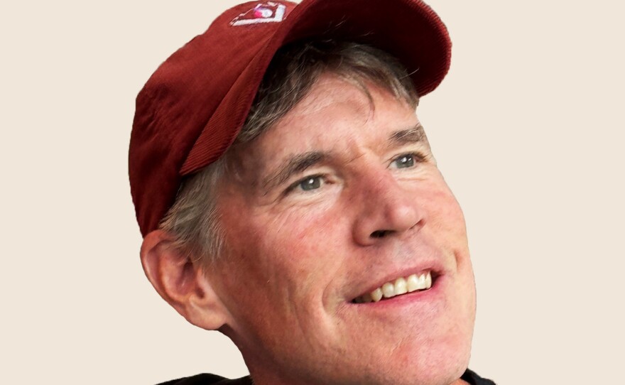 A smiling man wearing a red baseball cap and grey shirt with black sleeves.