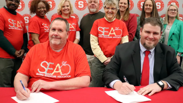 Members of the SEA stand for the signing of a new agreement which results in an increase in teacher pay scales in the district.