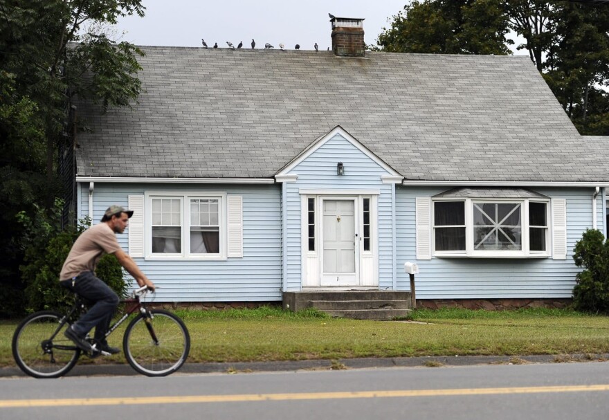 A man rides a bicycle by a house owned by the uncle of former New England Patriot's Aaron Hernandez, Thursday, Sept. 12, 2013 in Bristol, Conn. A group of people who all have ties to a small blue cape-style home in Bristol have become central figures in the investigations linking former New England Patriot Aaron Hernandez to two murder cases. (AP Photo/Jessica Hill)