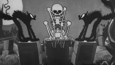 A cartoon skeleton surprises two black cats on top of tombstones, in a screenshot from the Walt Disney cartoon short The Skeleton Dance (1929). 