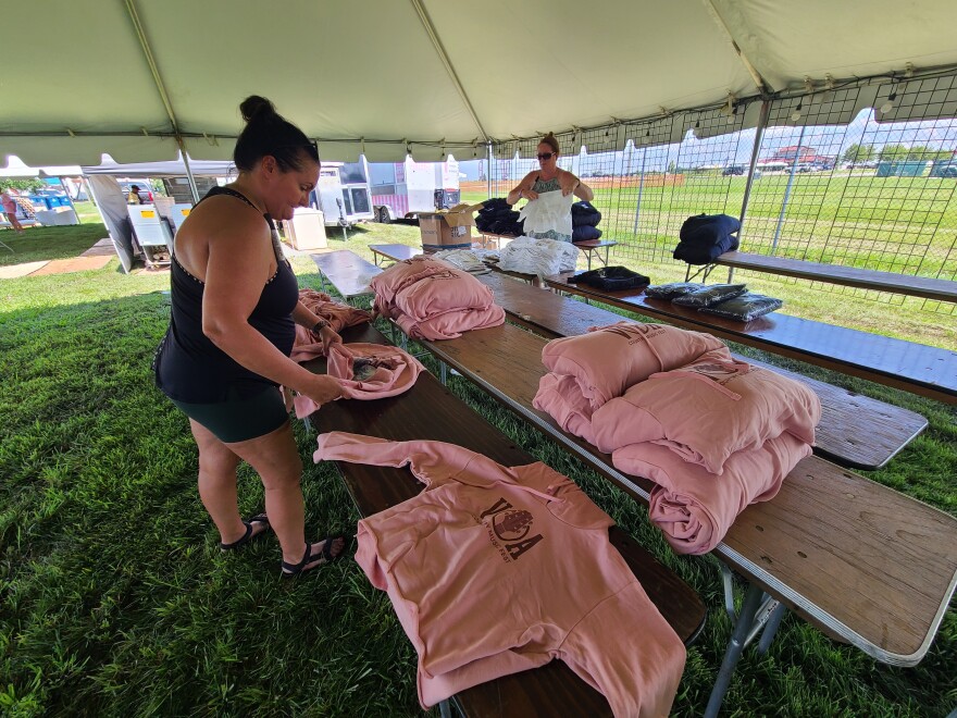 women fold shirts under a tent