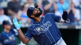 black baseball player in a blue Rays jersey and helmet celebrates by looking skyward with his arms out to each side 