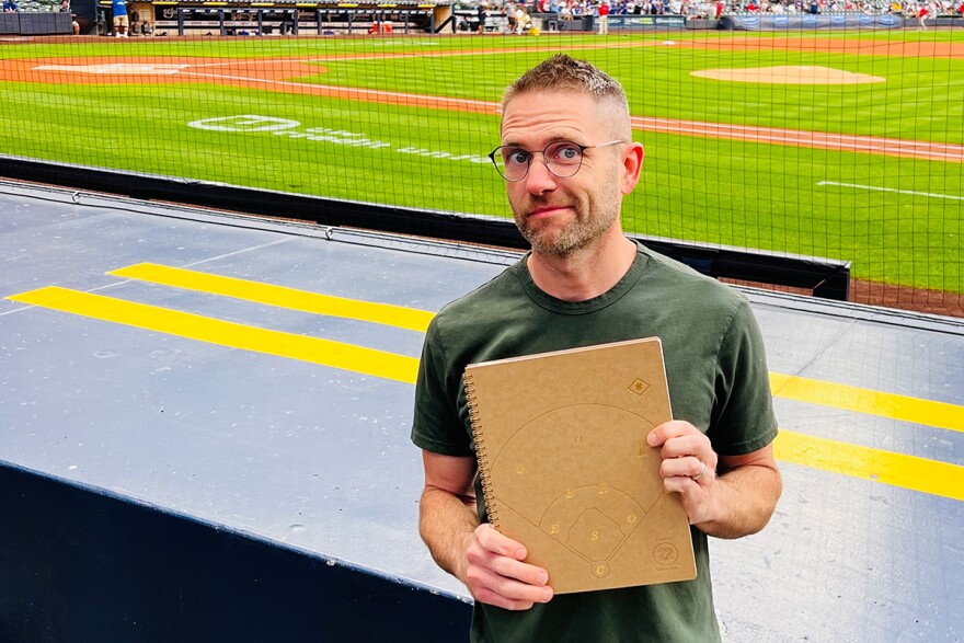 Numbers Game co-owner, John Kuehl, holds up his personal baseball scorebook before a game at American Family Field.