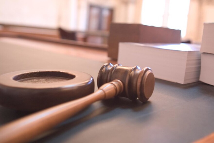 A brown gavel lays next to a stack of white papers. They are all sitting on a gray desk.