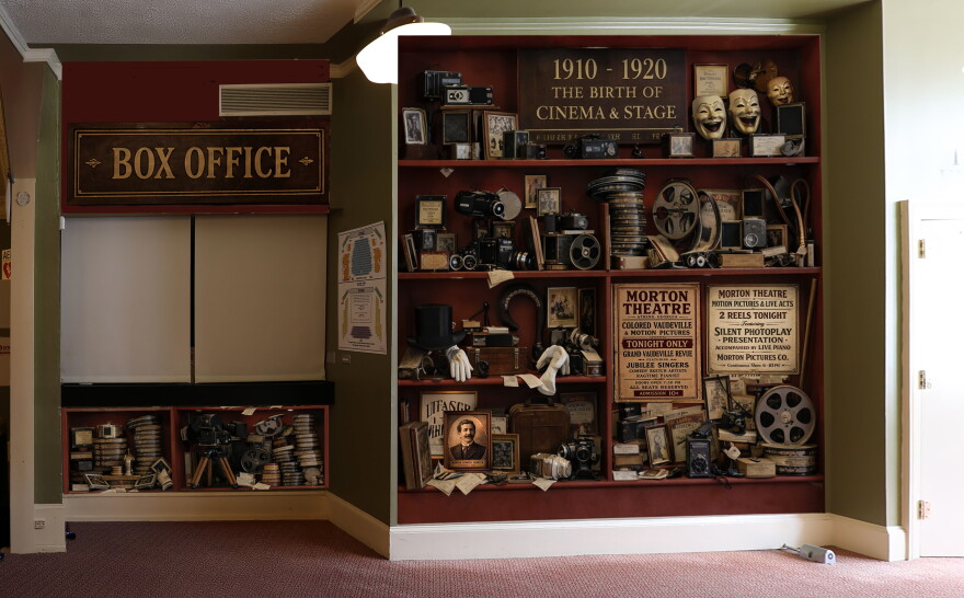 A wall display featuring vintage film equipment, posters and photographs beside a box office window.
