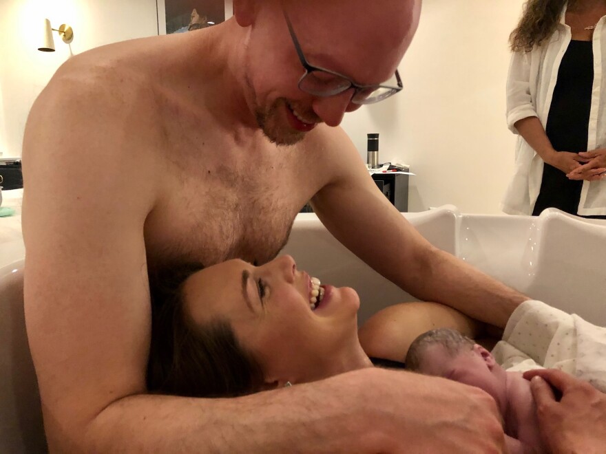 two parents smile at one another, holding a newborn baby