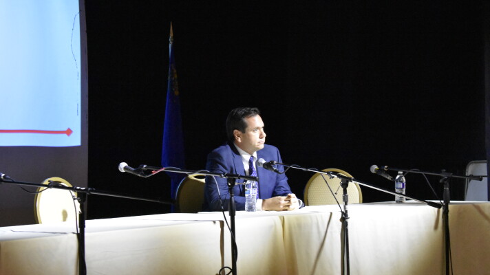 Cisco Aguilar sits at a long table with microphones by himself. 