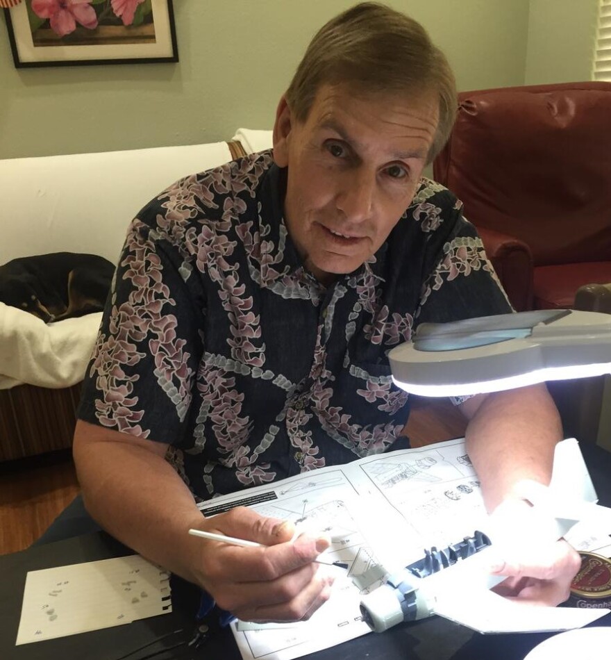 Jack Hall makes a model airplane in his room at Abode Contemplative Care for the Dying. The household dog, Sadie, rests on the couch behind him.