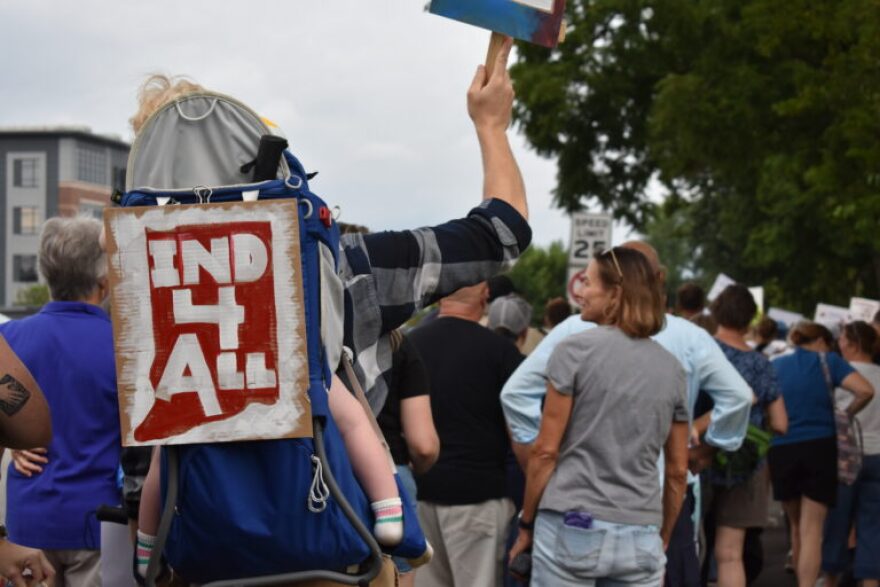 A pro-immigrant protester with an “Ind 4 All” sign marches with a child through Fishers on Saturday, Aug. 1, 2026.