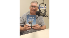 Daniel Grzywacz holding his book learn grow give, with a WGVU branded microphone near his face
