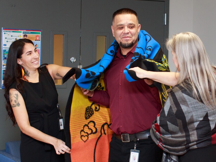 Native and Strong Crisis Counselor Robert Coberly is blanketed by Mia Klick, (left) a Native and Strong Lifeline coordinator, and Vicki Lowe, (right) executive director of the American Indian Health Commission for Washington state, during a blanket ceremony for the launch of the Native and Strong Lifeline. (Photo courtesy: Heaven Arbuckle-Hatchett)