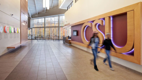 Two students walk past the letters C S U which are on the wall in a university building. 