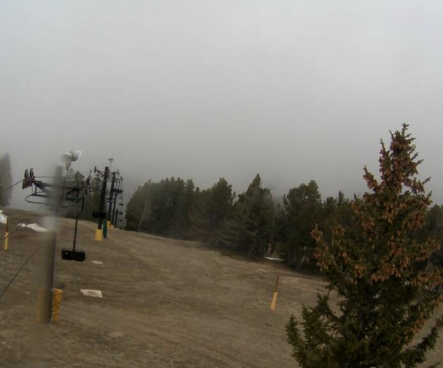A barren ski hill with one patch of snow and almost all grass.