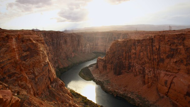 The sun shines on a river flowing through a deep red rock canyon