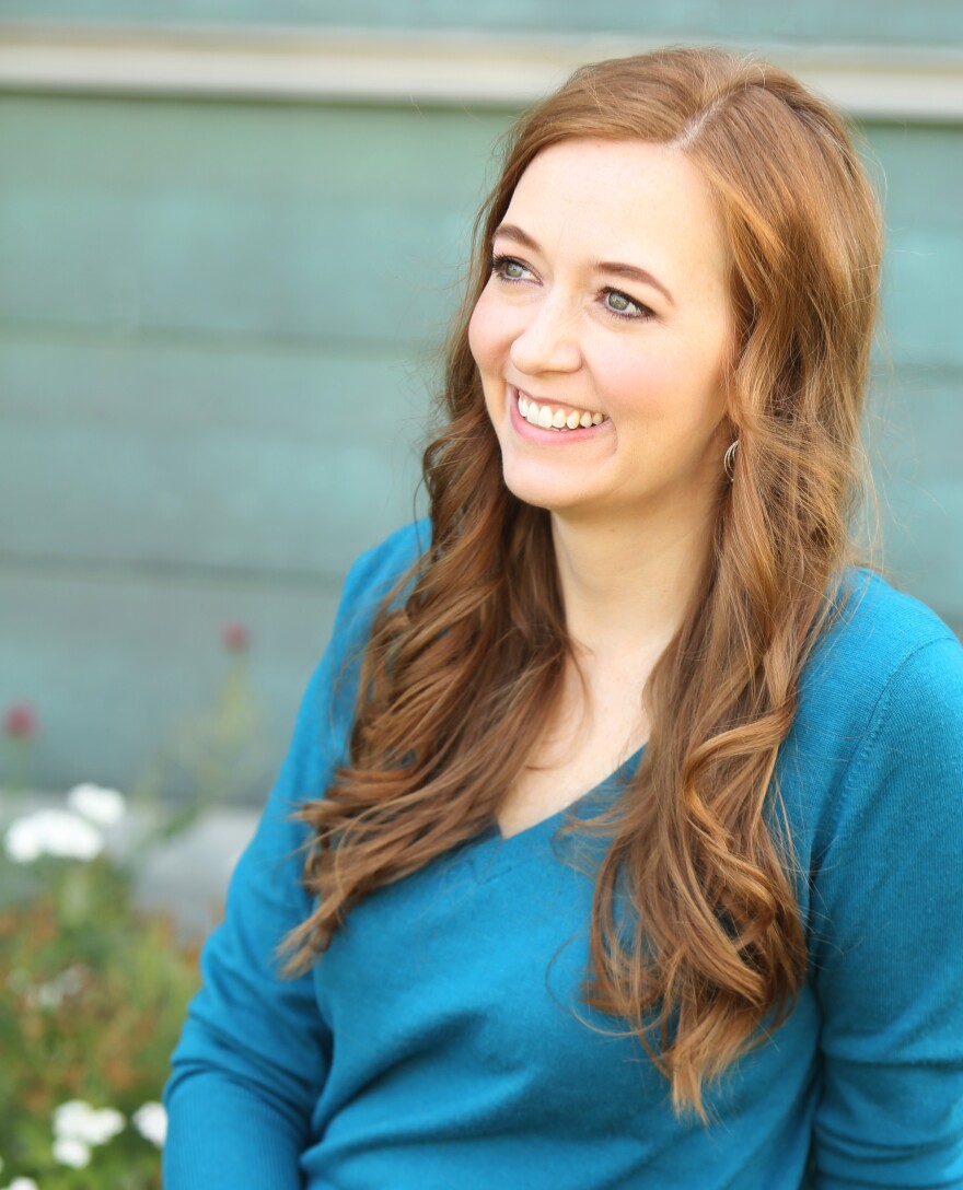 Shannon Hale, a white woman with brown hair, looks off to the side, smiling. She is wearing a blue shirt and sitting outside.