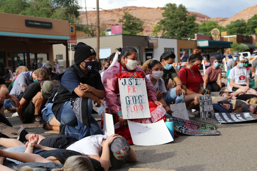 Photo of people sitting, kneeling and lying in a street with signs including “Justice For George Floyd.”