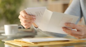 A womans hands open up an envelope while sitting at a glass table.