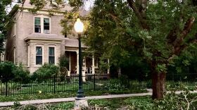 A photo of fall tree branches and a light post in front of a brown house.