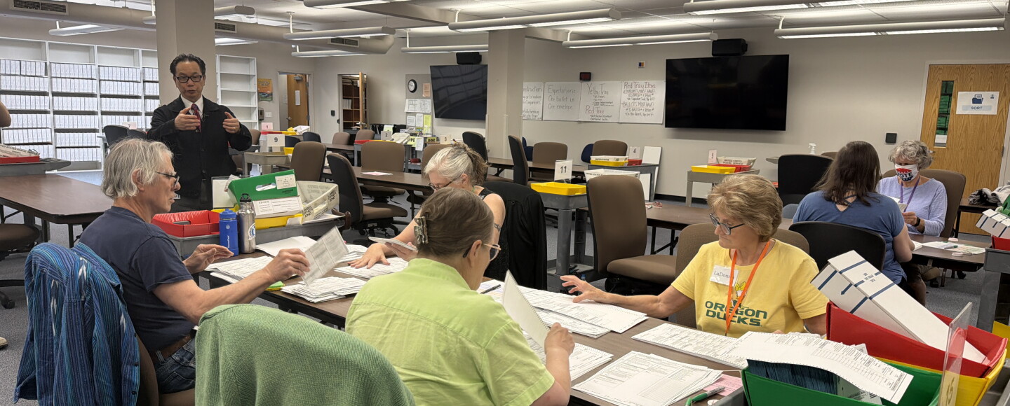 A group of Lane County Elections Office employees remove ballots from their envelopes and unfold them, preparing them to be scanned for vote counting, May 15, 2026.