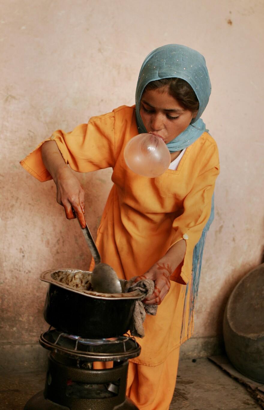 An Afghan girl blows bubble gum while cooking for her family in Kabul, 2007.