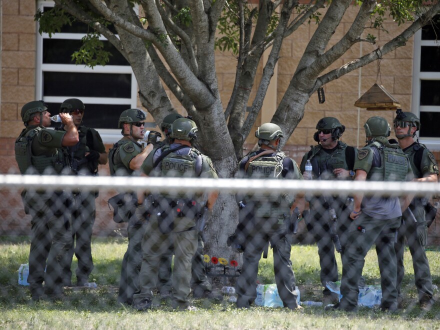 police officers gather between a fence and a building