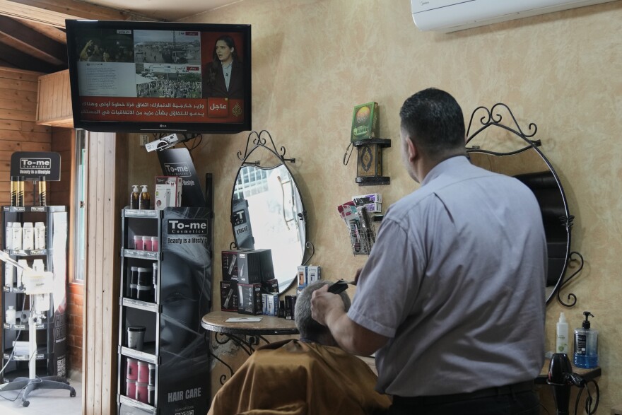 A barber cuts the hair of a customer as they watch the news on television following the announcement that Israel and Hamas have agreed to the first phase of a peace plan to pause the fighting, in Jerusalem, Thursday, Oct. 9, 2025.