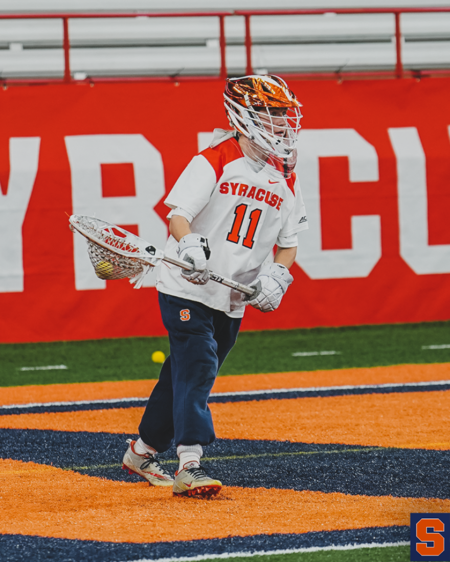 Syracuse goalie stands in front of the net holding stick and wearing a helmet.
