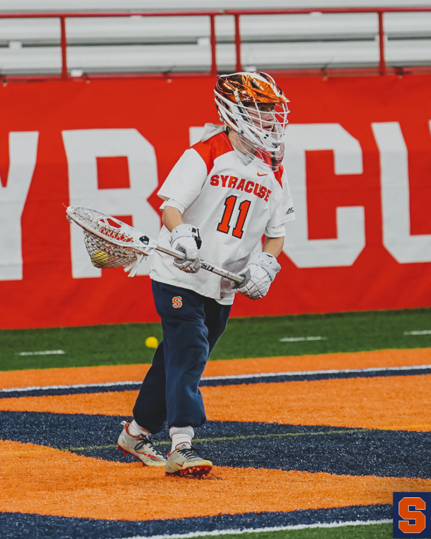  Syracuse goalie stands in front of the net holding stick and wearing a helmet.