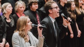Two soloists sing in front of a chorus of singers.