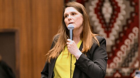 Woman in yellow shirt and black blazer talks into microphone