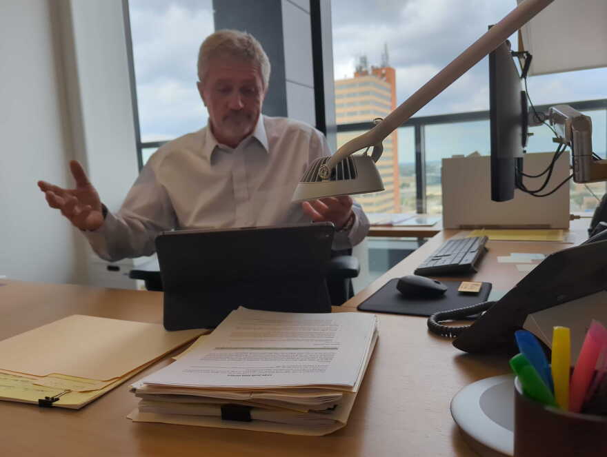 Tim Collins sits at his desk shrugging. On the desk is a stack of data center research.