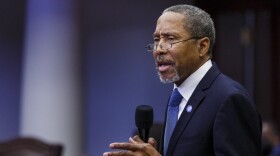 Elderly african american man in glasses and suit and tie speaks into microphone 