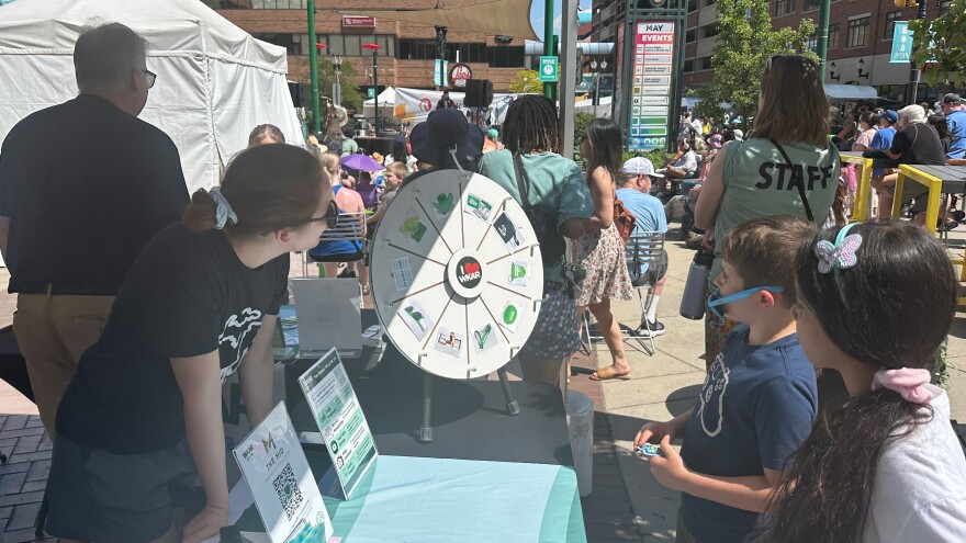 Jordan Nightingale, WKAR director of digital engagement, watches along as young attendees spin the prize wheel for free WKAR swag.