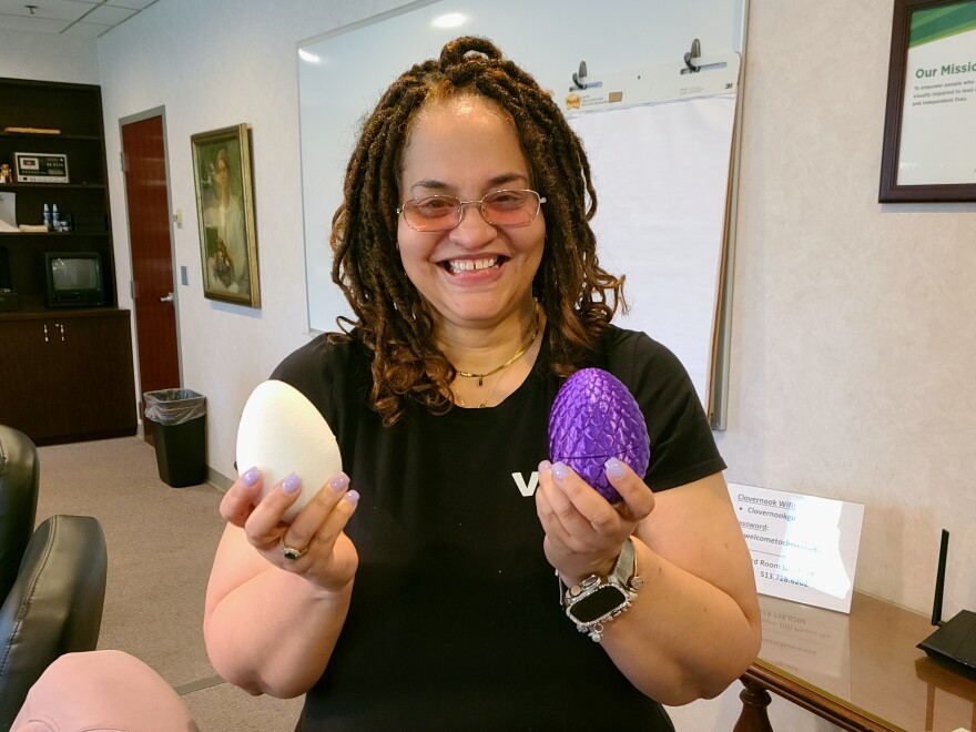 woman smiles to camera while holding two plastic Easter eggs.