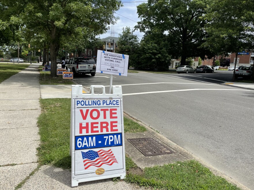 A placard that says "Vote Here" stands next to a street