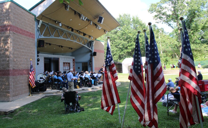 American flags line the grass beside the amphitheater stage, where band members perform under the pavilion roof.