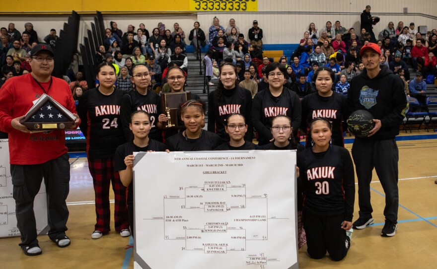The Kasigluk-Akiuk Lady Grizzlies pose alongside assistant coach Curtis Kassel (left) and coach Peter Nicholas (right) after winning the championship game at the 38th annual 1A Coastal Conference basketball tournament at the Warrior Dome in Bethel on March 3, 2026.