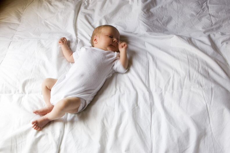 Newborn baby is shown sleeping on a bed.
