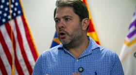 Gallego talking in front of flags