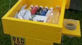 A yellow wooden box with paint supplies inside in a grassy outdoor setting