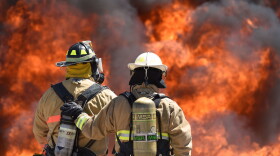 Two firefighters stand in front of a blaze